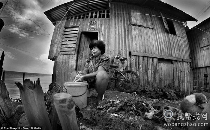 菲律宾的一位妇女正在大海一边的住宅旁洗涤东西，她周围布满碎石。.jpg